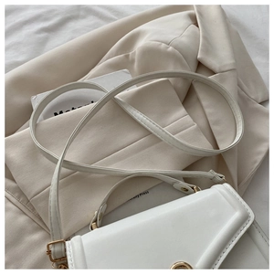 Close-up of white crossbody bag with gold round twist lock on beige blazer background