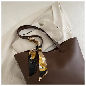 Close-up of a dark brown leather tote bag decorated with an elegant printed silk scarf