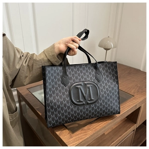 Close-up of black tote bag with M letter print texture and embossed logo detail