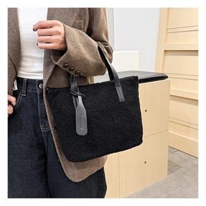 Detail of the black plush tote bag with a leather handle and a fashion tag accessory