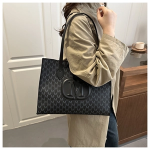 Close-up of black tote bag with embossed M pattern and circular logo detail