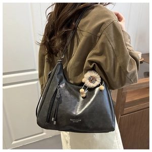 Detalle de bolso hobo negro con cremallera y colgante de oveja de peluche blanco