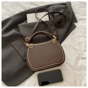 Detailed view of dark brown textured leather handbag with gold rings and U-shaped stitching