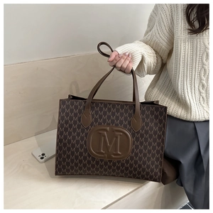 Macro detail of brown tote bag featuring all-over M pattern and leather logo patch