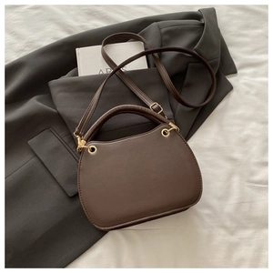 Detail of dark brown arc handbag with gold metal hardware on a grey blazer suit