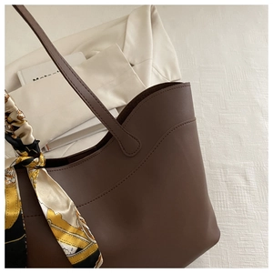 Macro view of textured brown tote bag with decorative silk scarf and shoulder strap detail