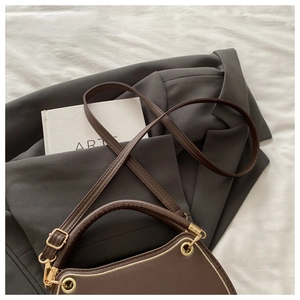 Detail of dark brown leather handbag with gold grommets on white fabric and blazer