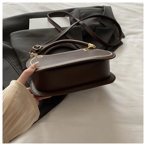 Detail of dark brown faux leather handbag with golden hardware and adjustable strap