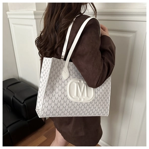 Vue latérale du grand sac cabas crème avec motif monogramme gris porté par un mannequin