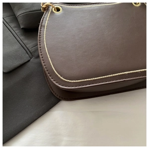 Detail of dark brown leather bag showing coarse yellow stitching and gold eyelet accents