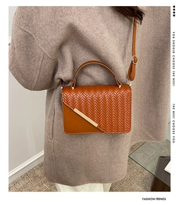 Detail einer braunen Tasche mit Webstruktur und Goldverzierung an einem Modell