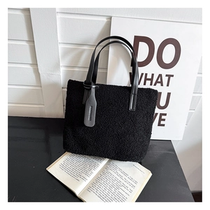 Detail of black plush bucket bag with leather strap and fashion tag on modern desk
