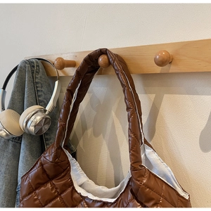 Detailed view of brown quilted tote bag showing padded texture on a wooden hook