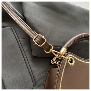 Detailed close-up of golden metal buckle and leather strap on a brown shoulder bag