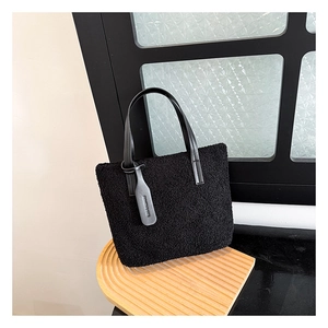 Detail of black faux fur bucket bag with smooth leather handles and embossed tag