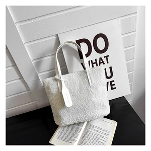 Close-up of a white plush teddy bucket bag with leather handles on a minimal black table