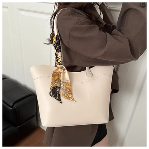 Chic beige tote bag with decorative printed silk scarf on handle, shown in shoulder wear