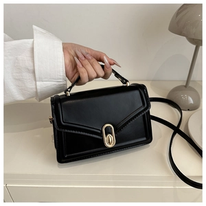 Detail of elegant black square leather handbag with gold metal lock on a white surface