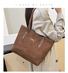 Detail of dark brown tote bag with suede texture and elegant gold bow metal accessory