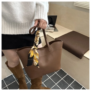 Brown leather tote bag with decorative silk scarf accessory shown in a casual lifestyle setting