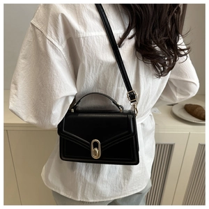Close-up of elegant black crossbody square bag with golden oval metal lock and top handle