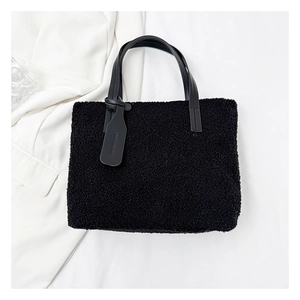 Close-up of black plush bucket bag with leather handles and embossed tag on white fabric