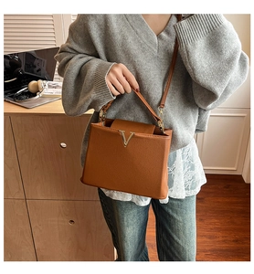 Détail d'un sac à main en cuir caramel avec un accessoire métallique en forme de V doré