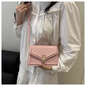 Pink crossbody bag with gold U-shaped buckle on model in minimalist setting