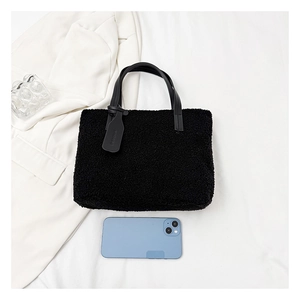 Close-up of black fuzzy lamb wool tote bag with leather handles on white fabric