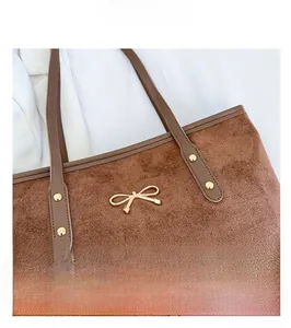 Détail d'un cabas en daim marron avec ornement nœud doré et rivets métalliques