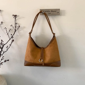 Brown suede hobo bag with leather trim and metal ring on minimalist cream background