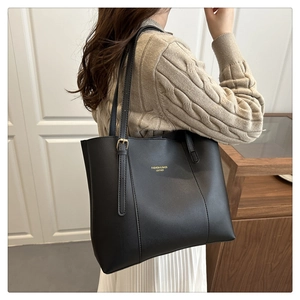 Detail of minimalist black leather tote bag with gold lettering and adjustable buckle
