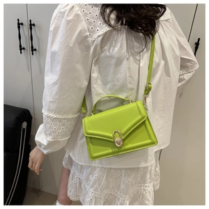 Detailed view of neon green mini crossbody bag with metal twist lock on white lace dress