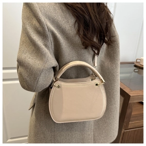 Detail view of beige leather crossbody bag with gold trim on brown wool coat background