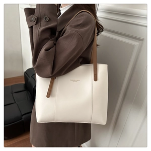 Close-up of white leather tote bag with brown straps and stylish text on wool coat