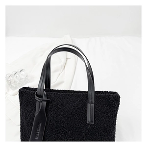 Detail of black faux shearling bucket bag with leather handle and fashion tag