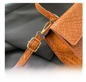 Gros plan sur la boucle dorée et la bandoulière en cuir tressé d'un sac orange