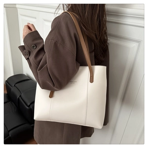 Detail of white tote bag with brown leather straps and fashion text on woolen coat