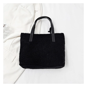 Close-up of black fleece bucket bag with leather handles on minimalist white background