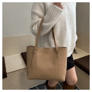 Detail of beige leather tote bag with gold lettering shown on model in white knitwear