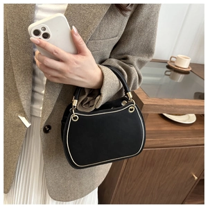 Detail of black matte leather handbag with gold accents held by model in casual setting