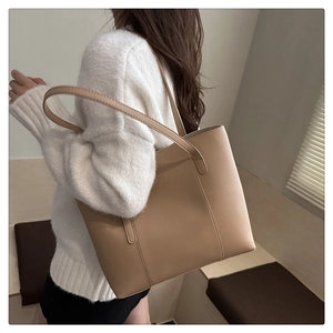 Detailed shoulder view of a beige leather tote bag with long slim handles and subtle texture