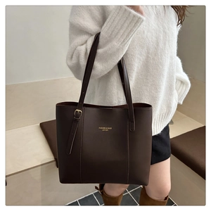 Close-up of brown leather tote bag with gold lettering and buckle detail on white sweater