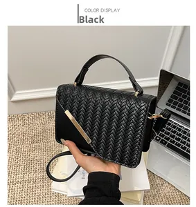Detail of a black woven crossbody bag featuring a golden metal buckle and sleek top handle