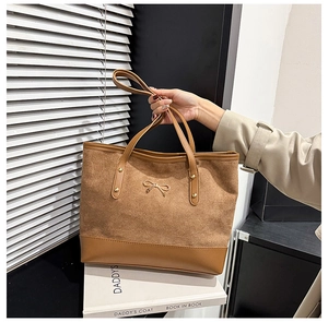 Detail of brown suede tote bag with metallic bow and rivet accents for office commute