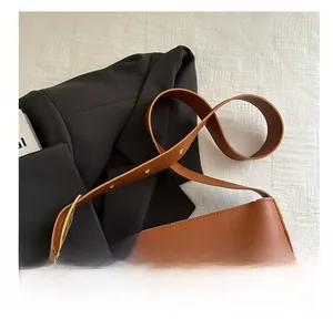 Close-up of the wide brown leather strap with precise stitching on a minimalist bucket bag