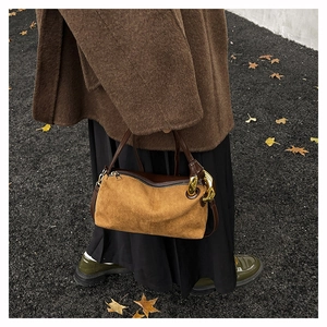 Detail of vintage brown suede shoulder bag with thick gold chain against autumn leaves