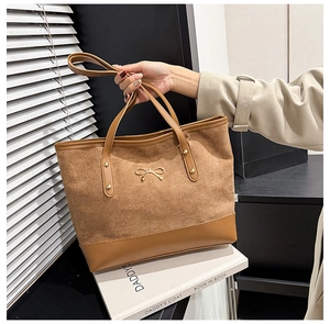 Close-up of brown tote bag with matte texture, gold bow clasp and smooth leather trim