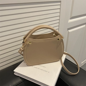 Elegant beige top-handle crossbody bag with gold hardware on a minimalist background