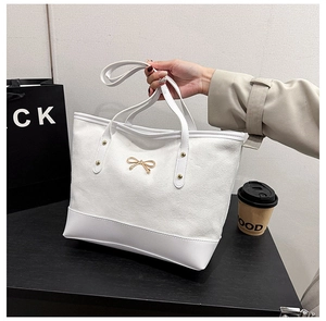 Détail du sac cabas en toile blanche avec nœud doré et anses en cuir porté à la main